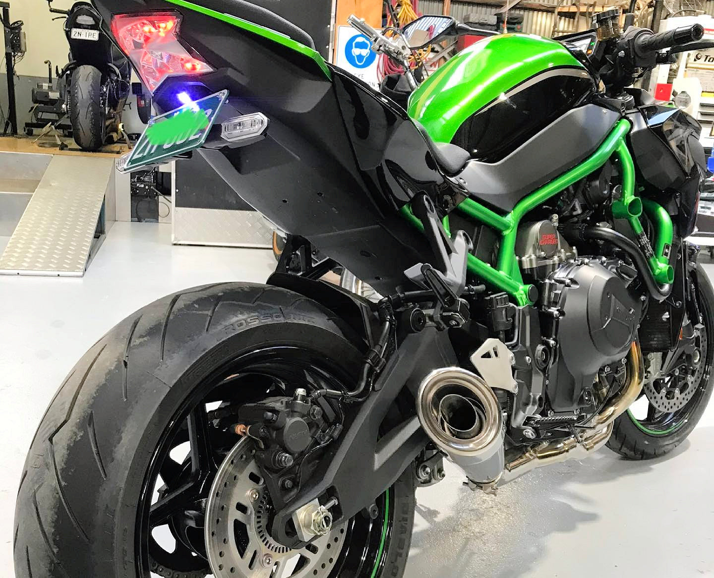 Rear view of green sport bike, showing exhaust and tire.