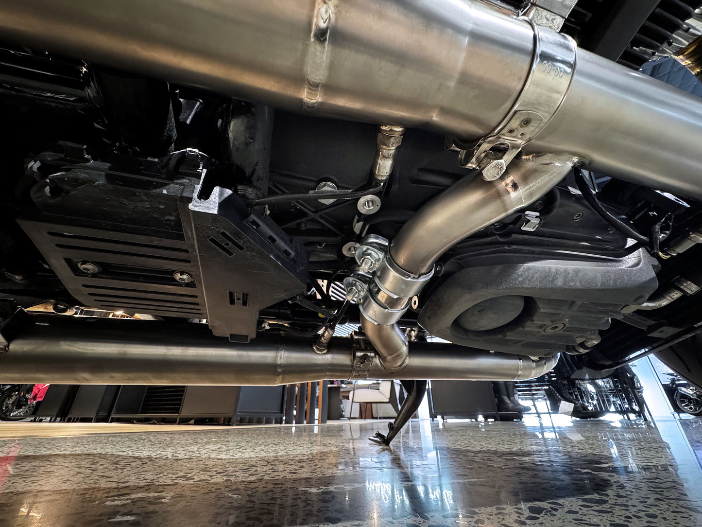Detailed view of a car's exhaust pipe, highlighting its shiny metal finish and connection to the vehicle's undercarriage.