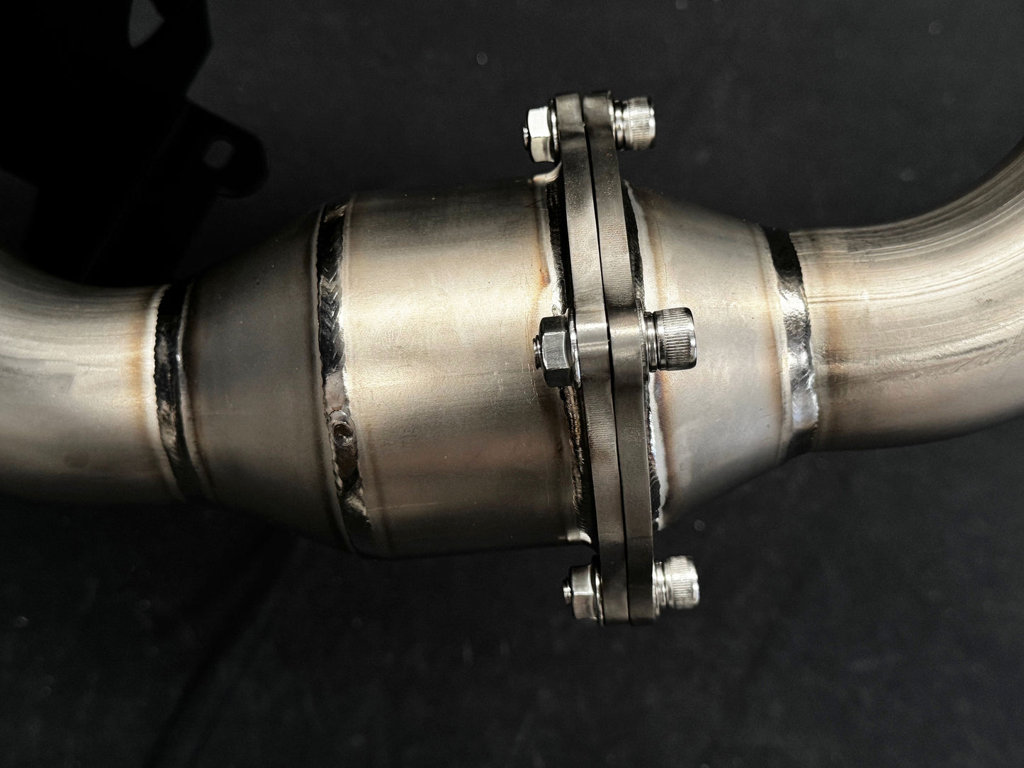 Detailed metallic motorcycle exhaust system close-up against dark.
