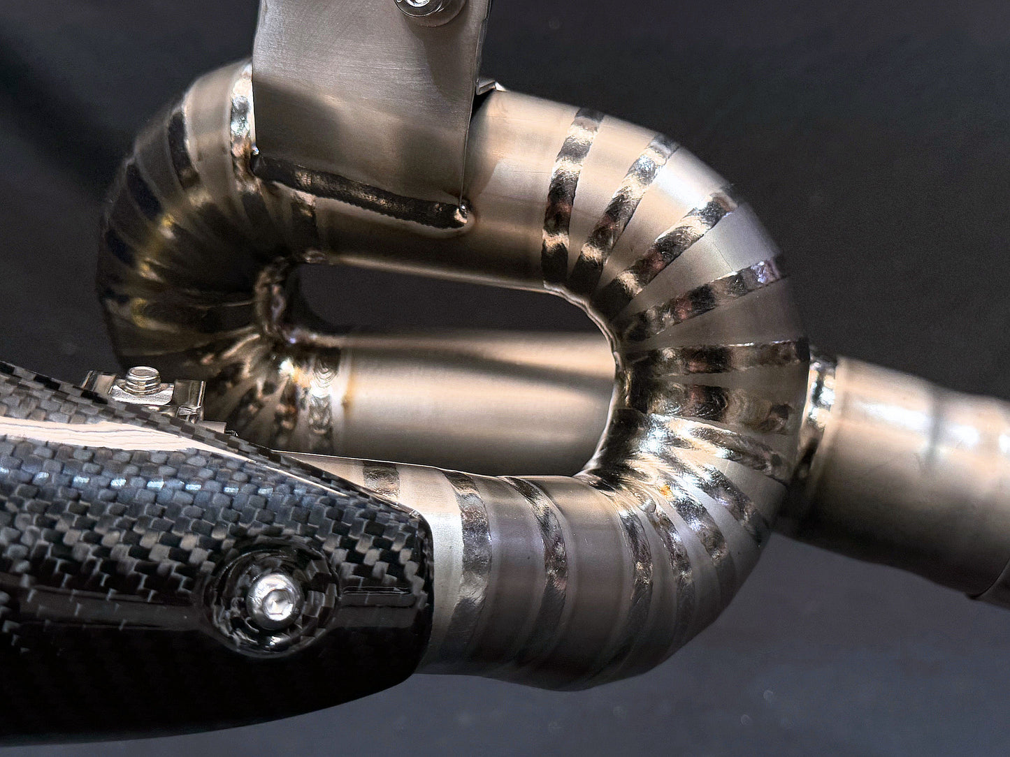 Metallic motorcycle exhaust reflecting light, close-up.
