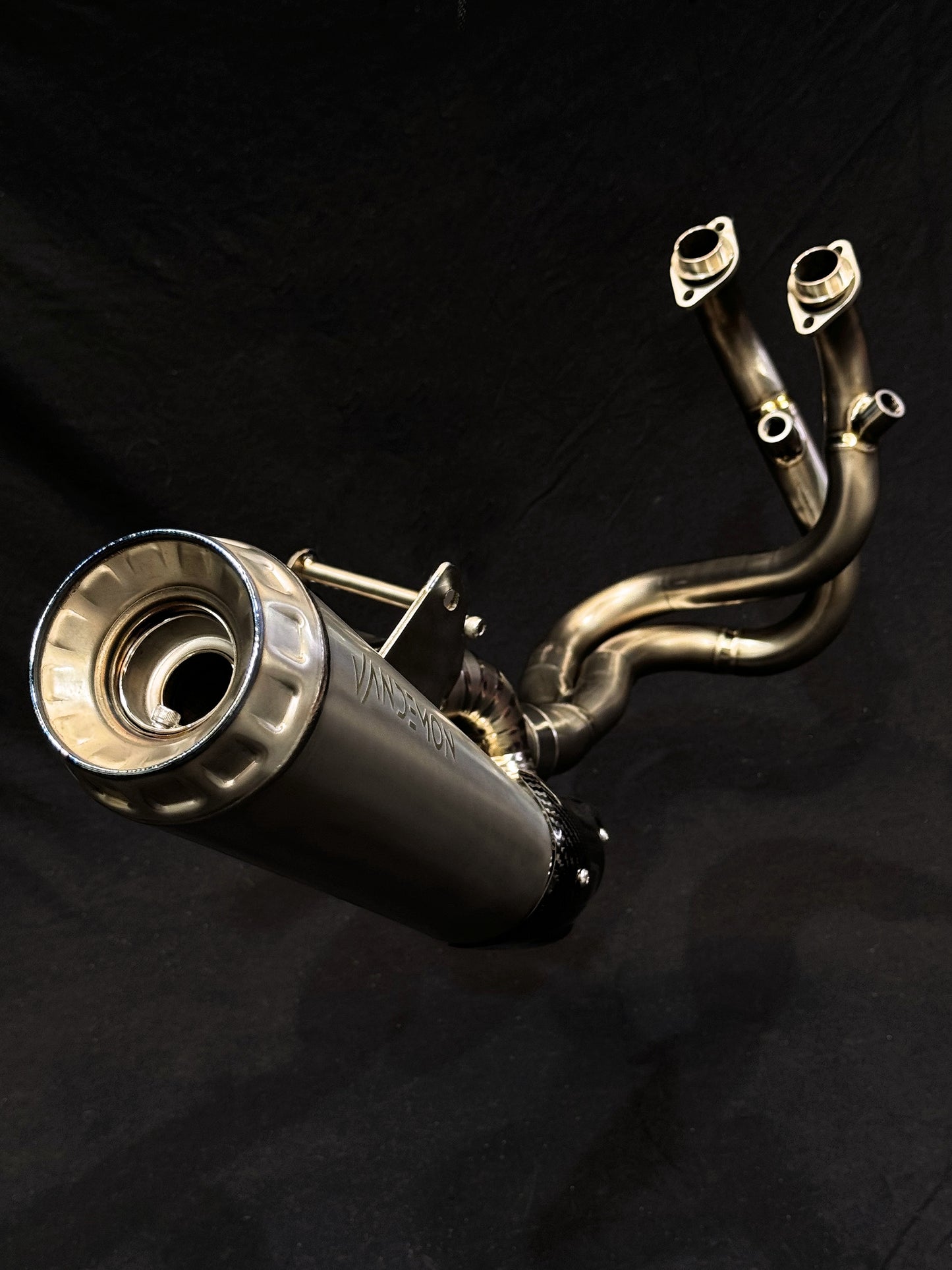 Sleek motorcycle exhaust system reflecting light on dark background.