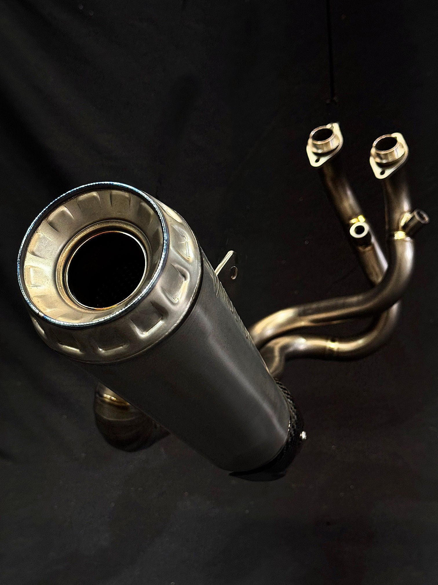Intricate detailing on dual-exhaust motorcycle system in dark setting.