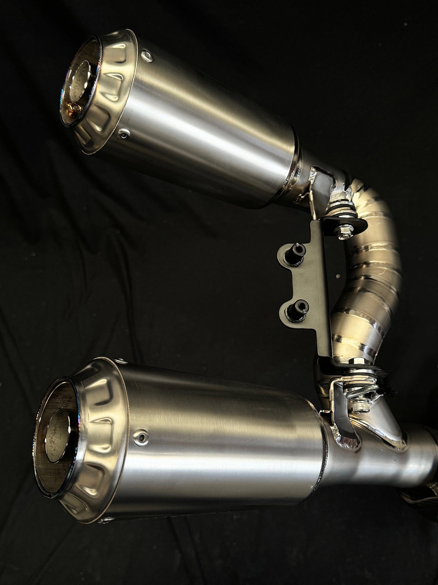 Close-up of dual-exhaust motorcycle exhaust system against dark background.