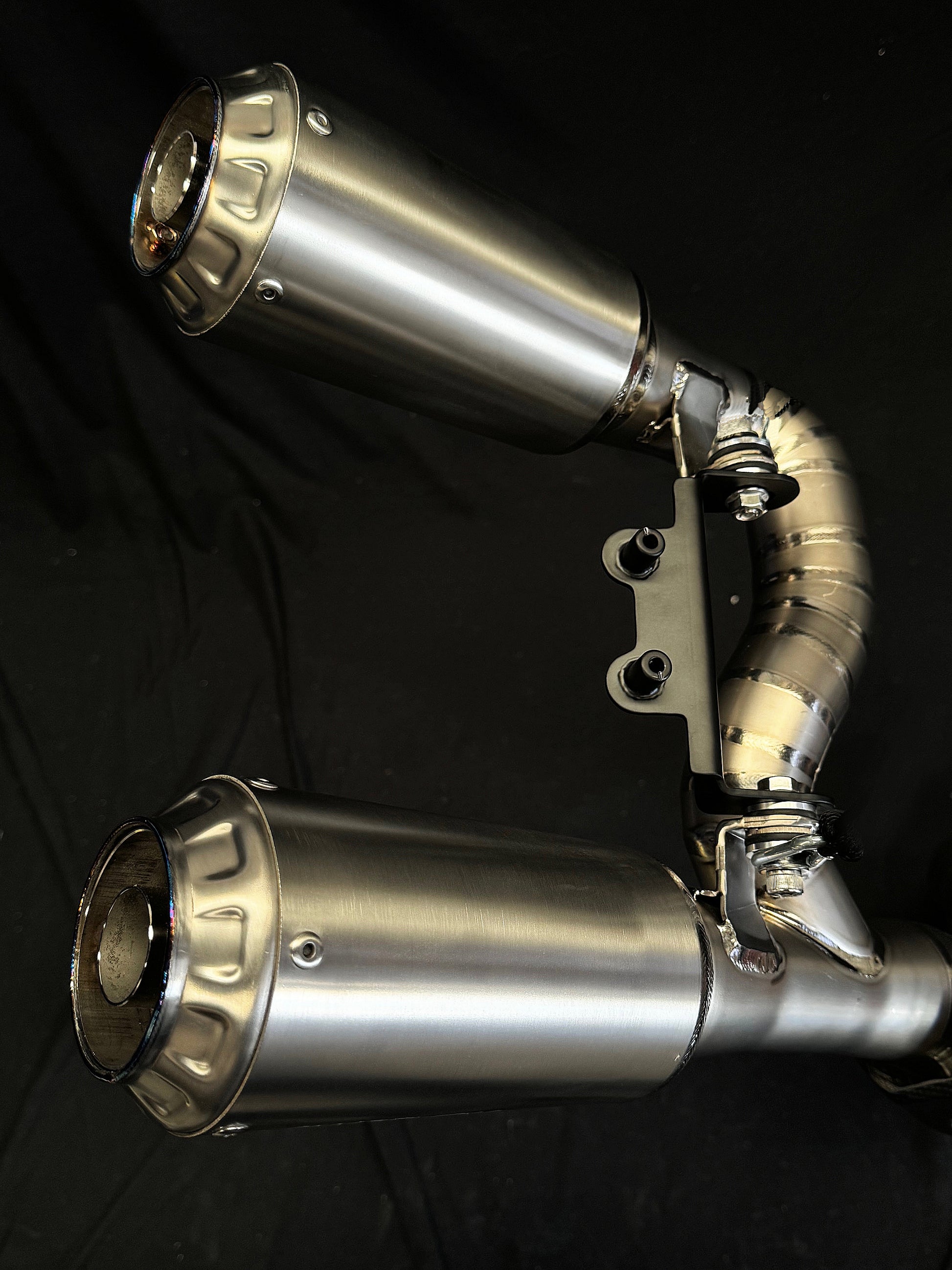 Close-up of dual-exhaust motorcycle exhaust system against dark background.