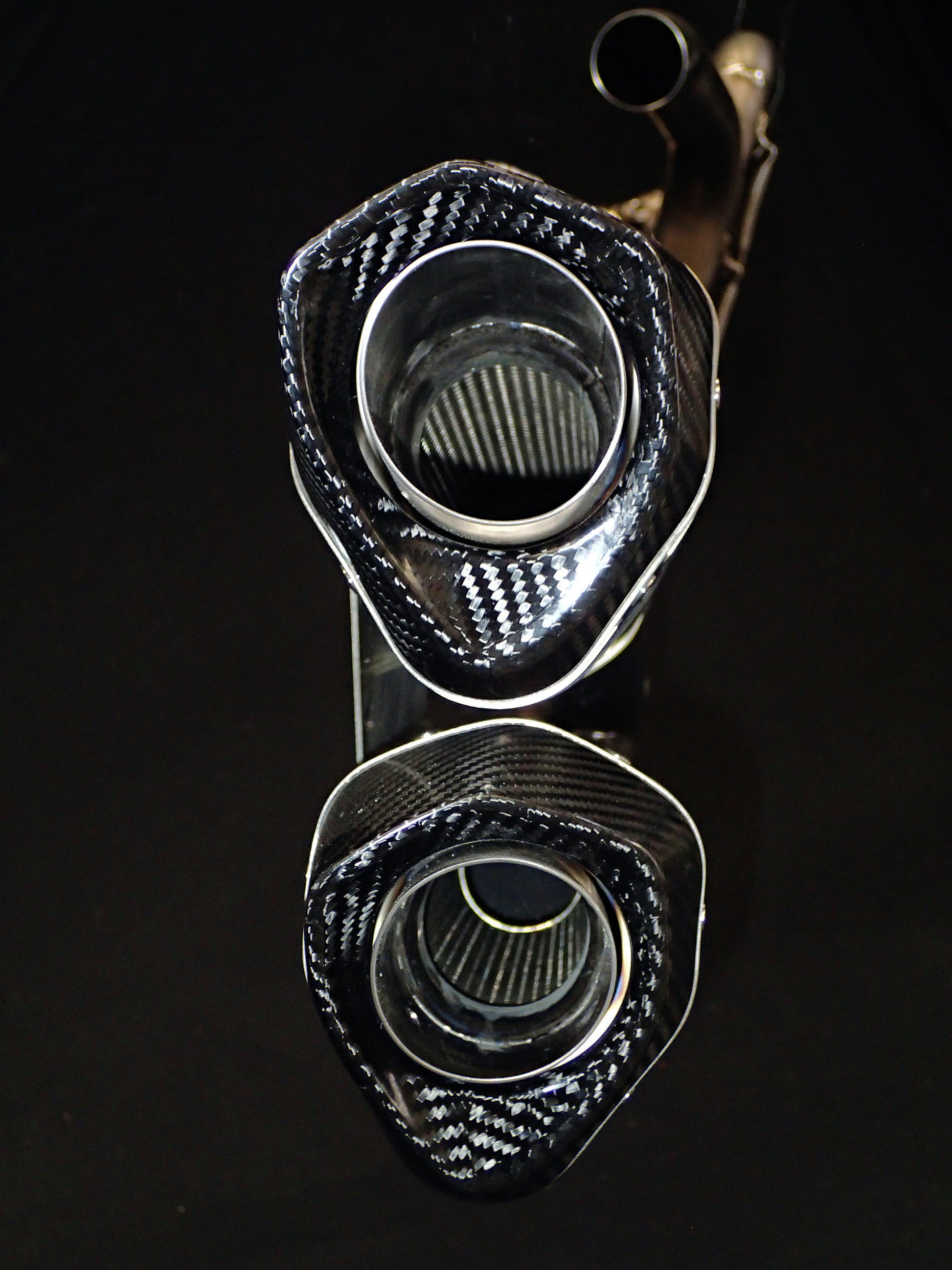 Intricate dual-exhaust system for motorcycle against dark background.