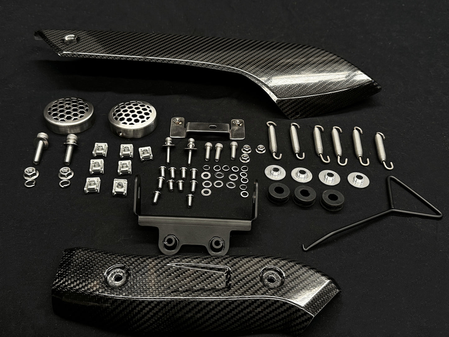 A collection of metal and carbon fiber automotive parts arranged on a dark surface.