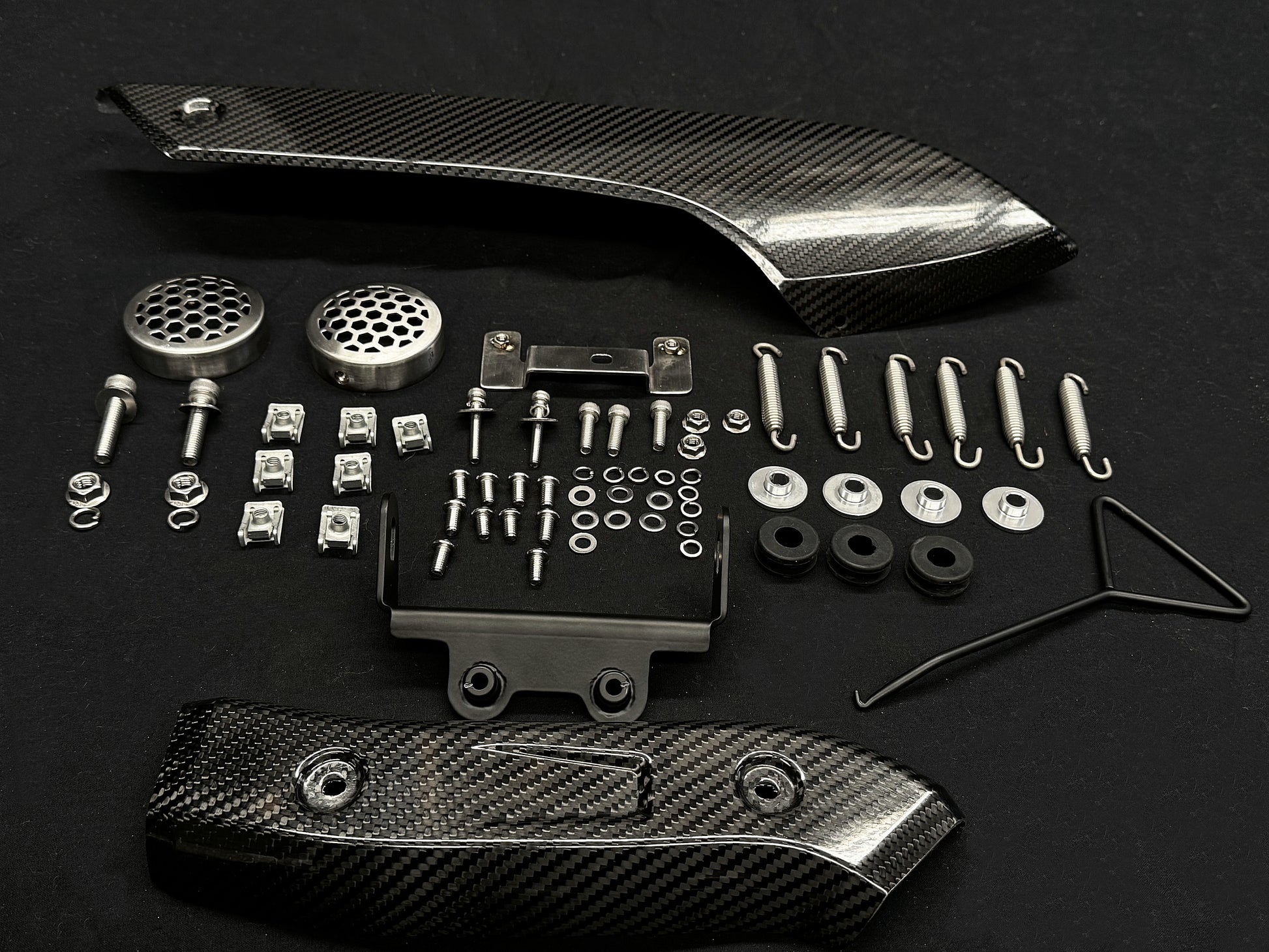 A collection of metal and carbon fiber automotive parts arranged on a dark surface.