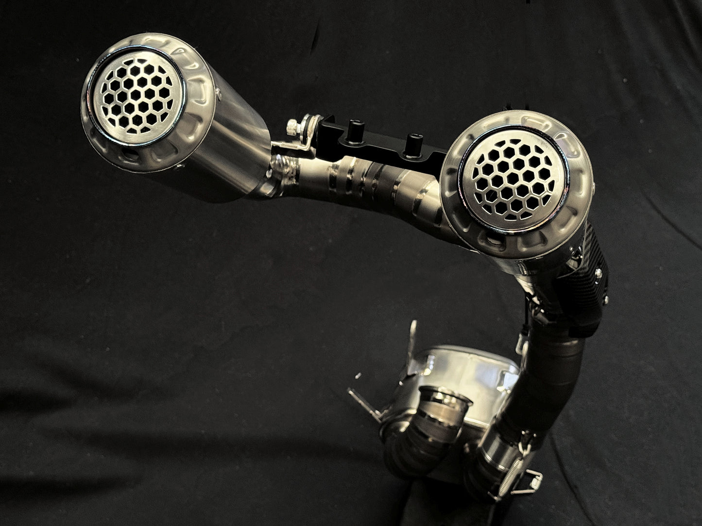 Close-up of a shiny, dual exhaust system with metal pipes and circular vents against a dark background.