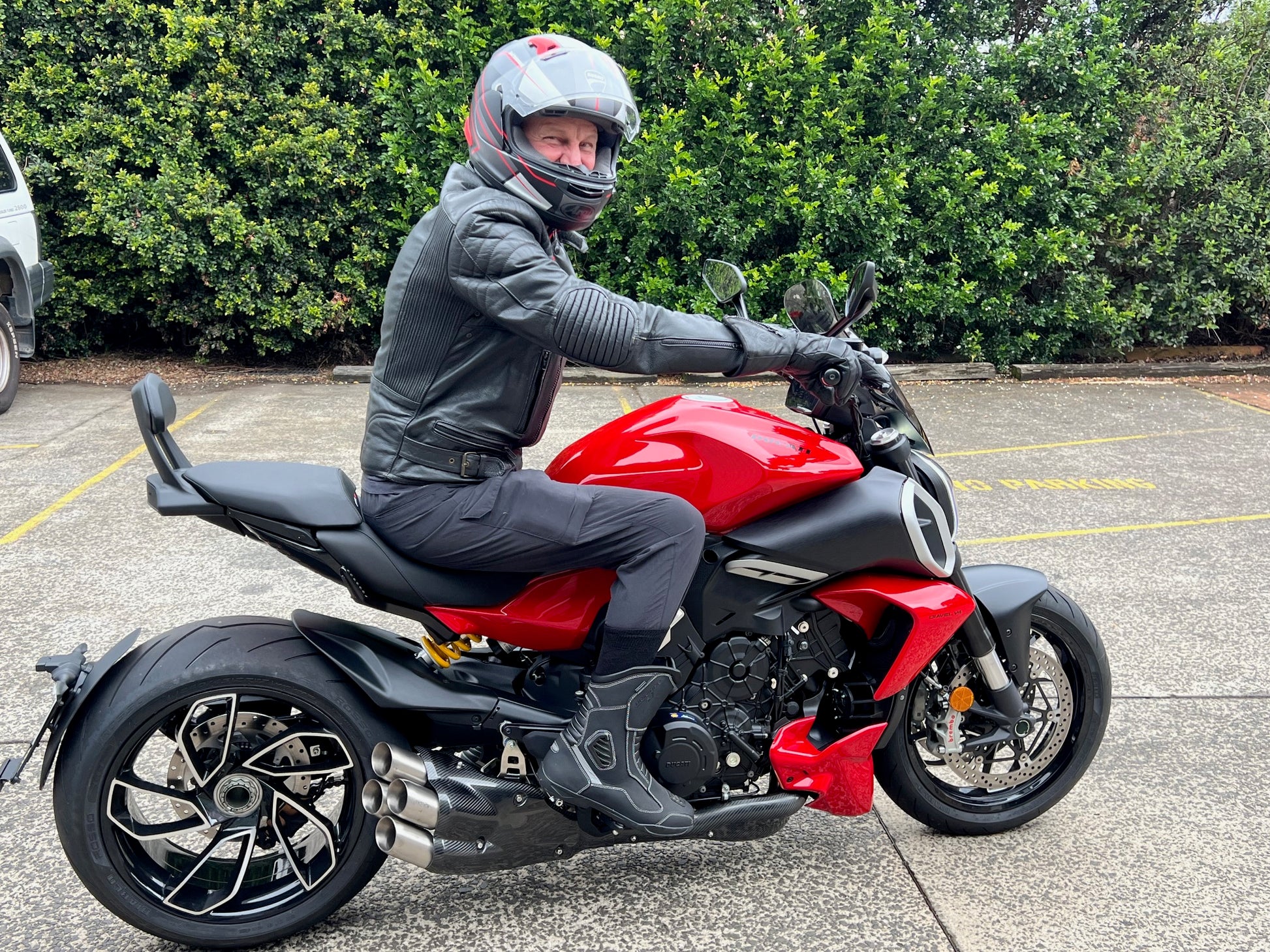 A man in a helmet and leather jacket rides a vibrant red motorcycle