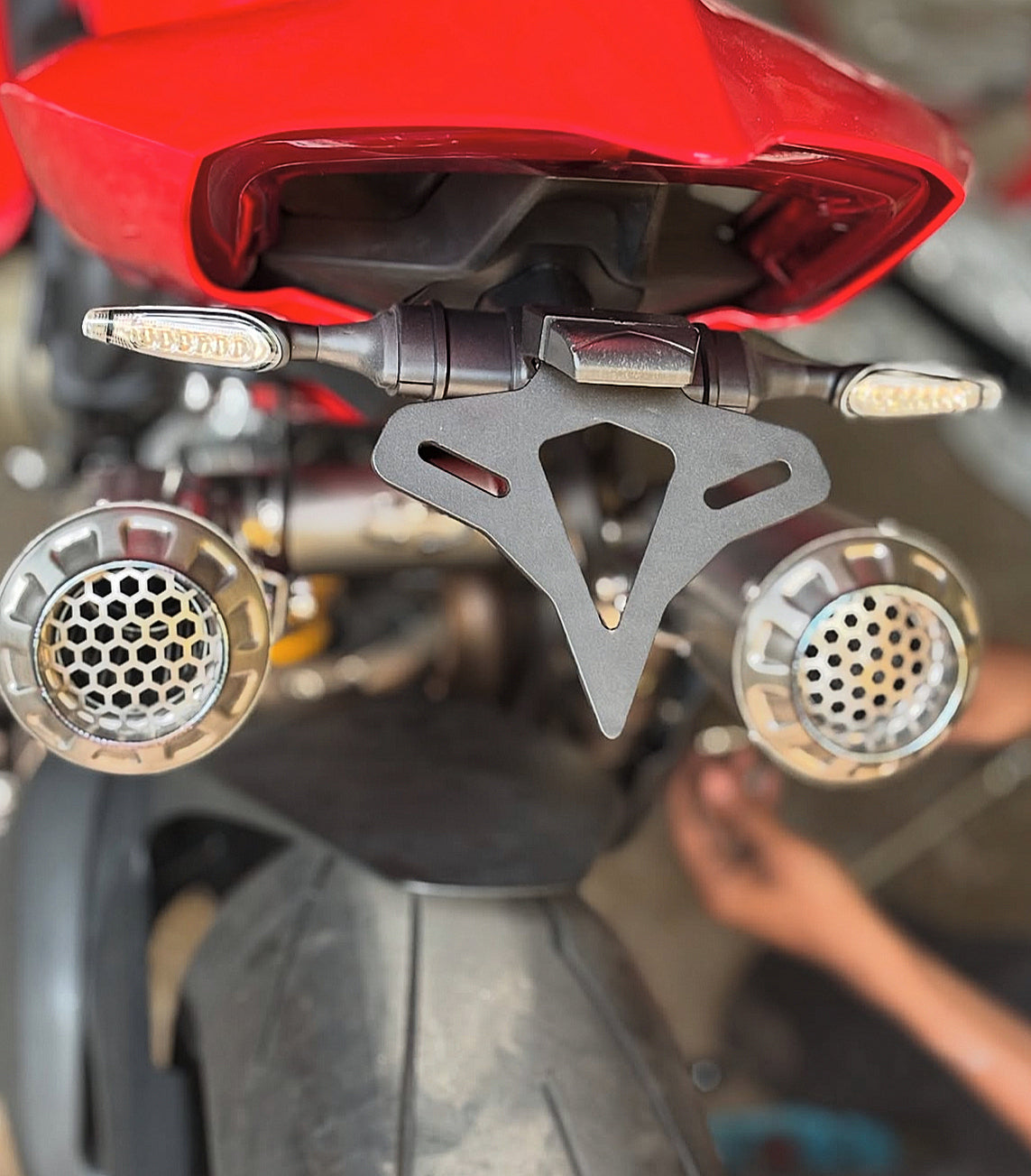Close-up view of a red motorcycles rear, featuring twin exhaust pipes and a license plate bracket.