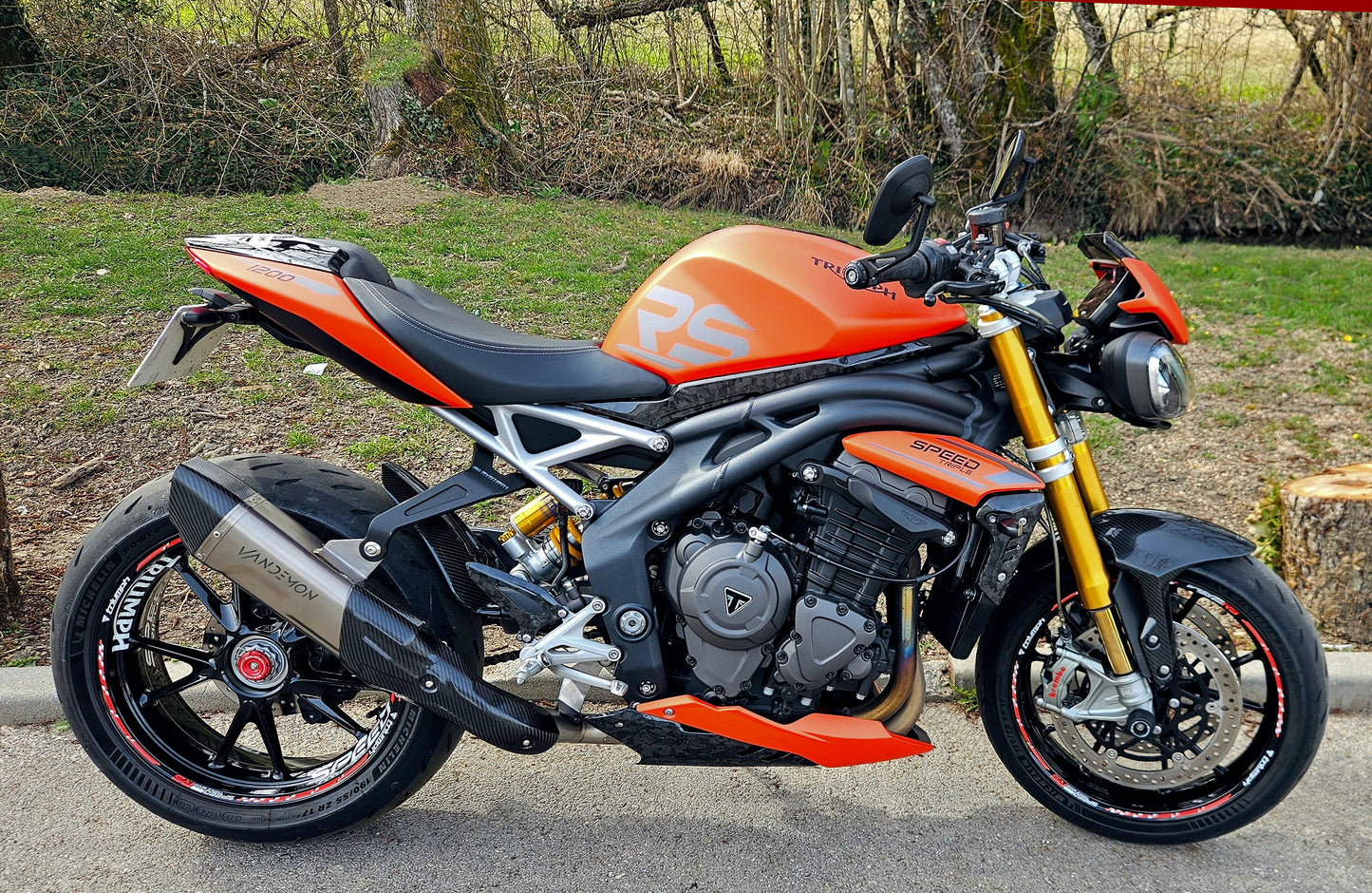 A bright orange motorcycle with RS on the side is parked on a road.