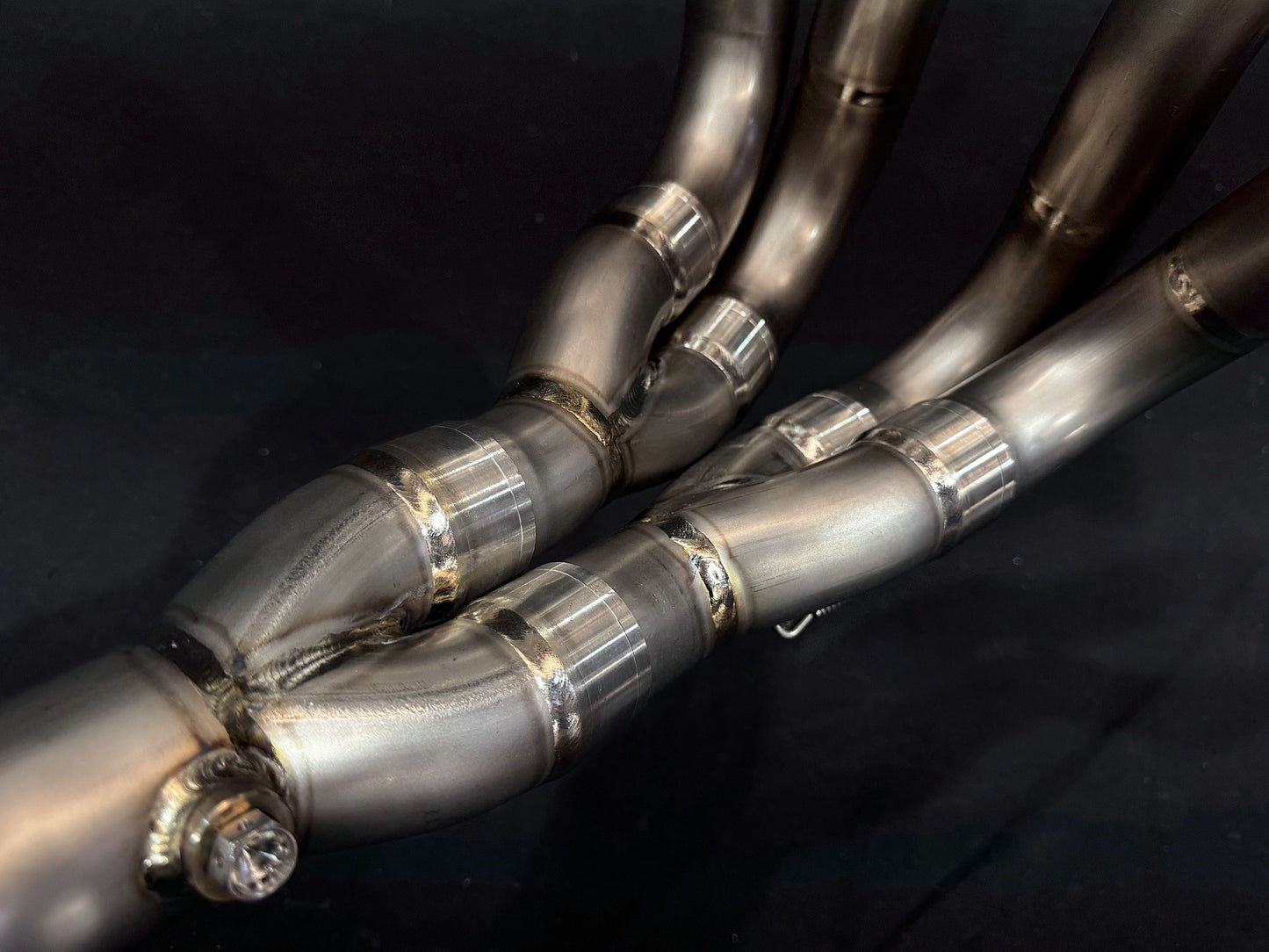 Intricate dual-exhaust system for motorcycle against dark background.