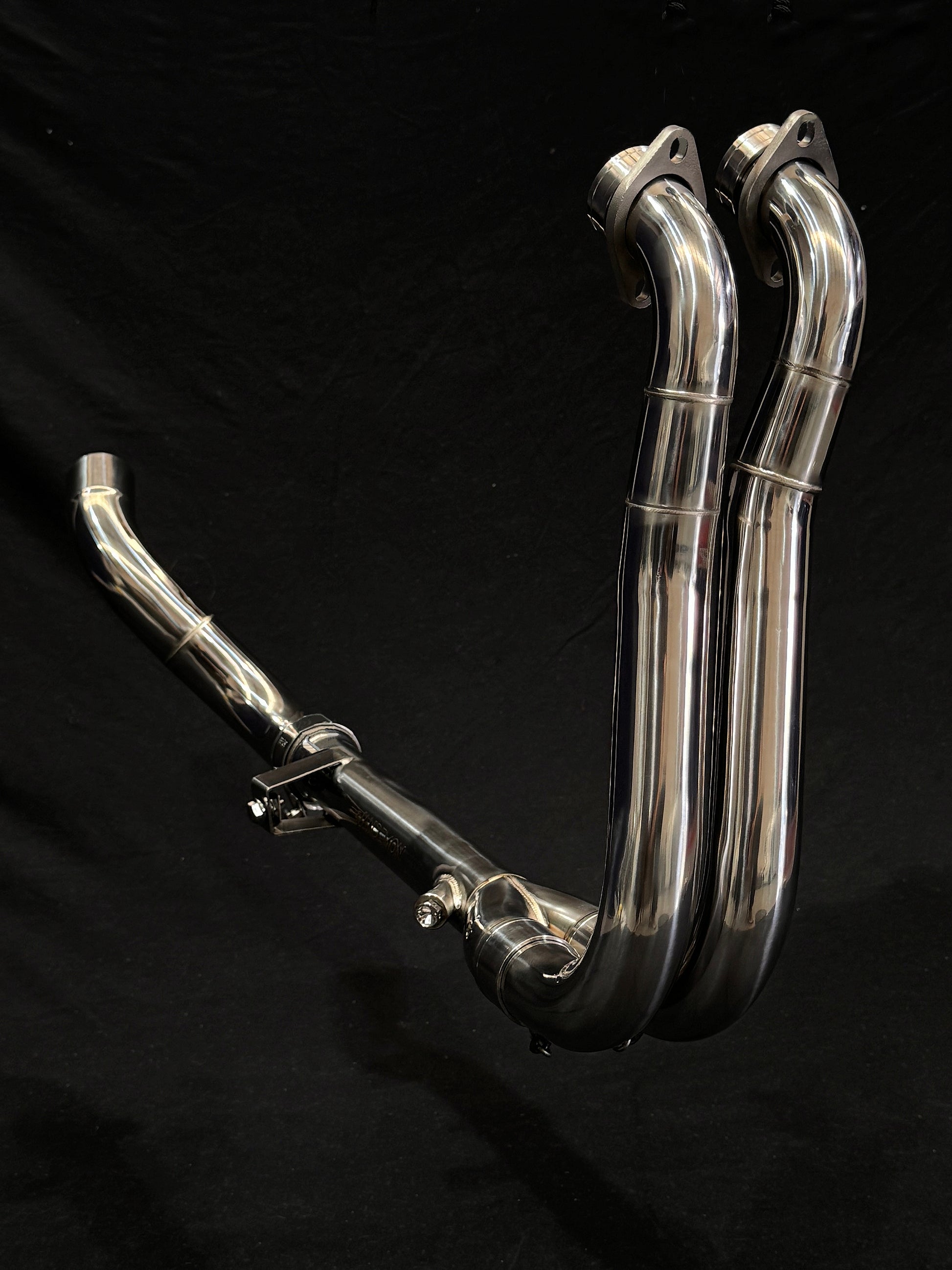 Shiny dual-exhaust motorcycle system against dark backdrop.