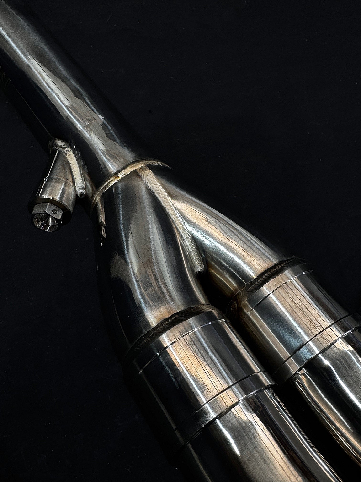 Metallic, sleek motorcycle exhaust close-up against dark background.