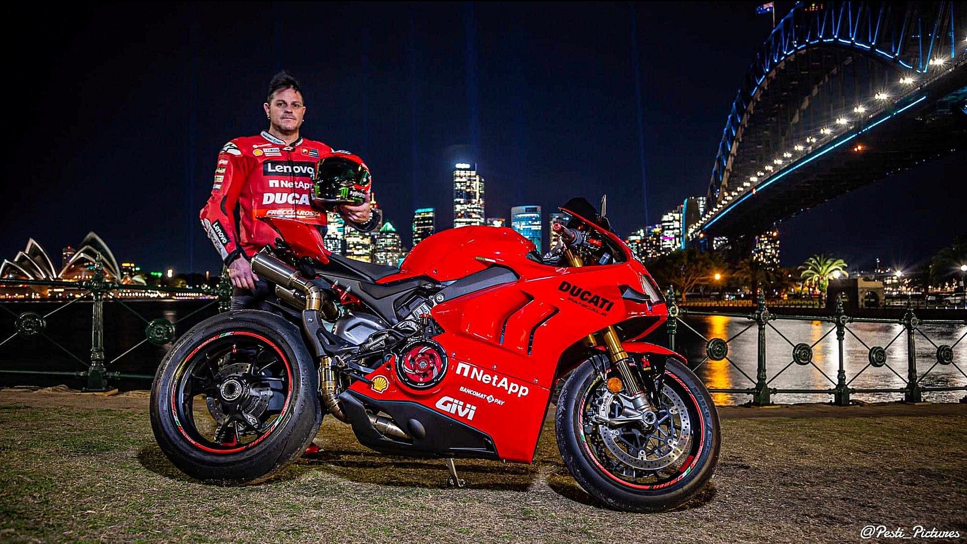 A man standing beside a red motorcycle.