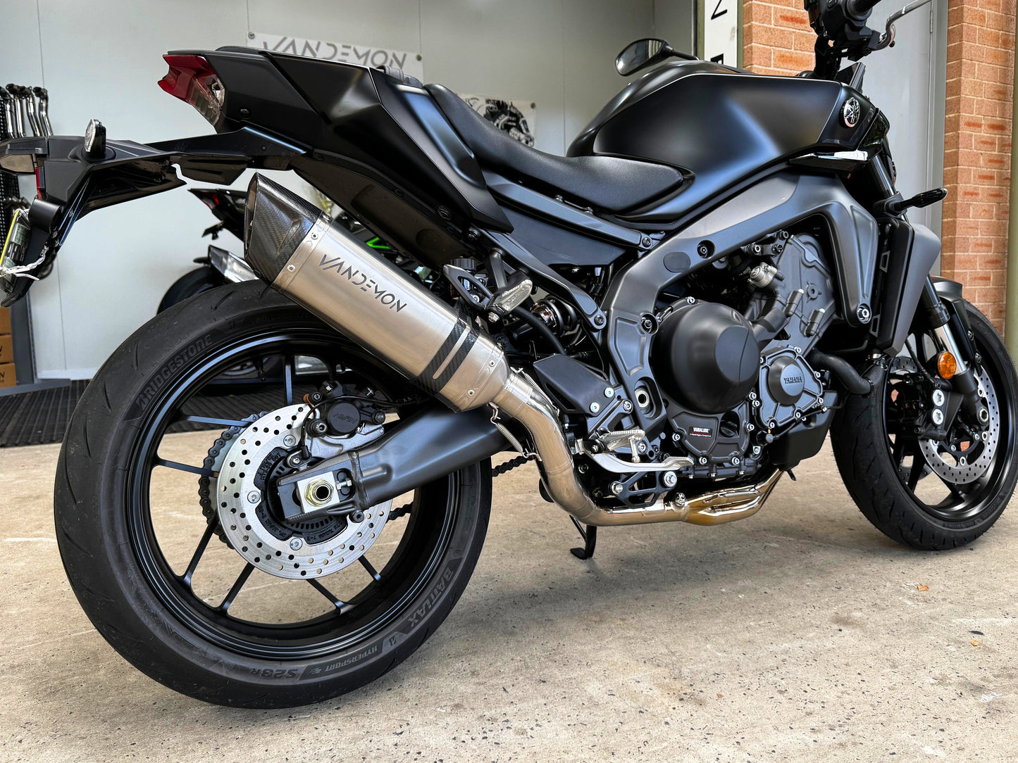 Grey sport motorcycle parked indoors, Vandemon exhaust visible.