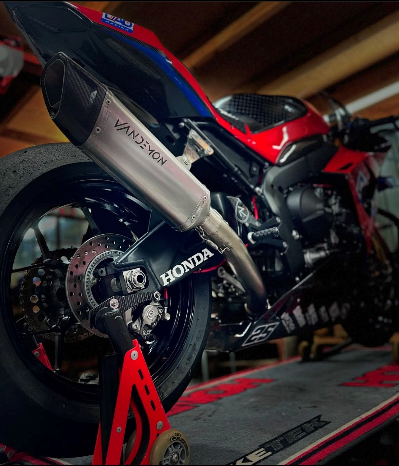 A motorcycle resting on a stand in a garage, highlighting a tidy environment filled with tools and motorcycle gear.
