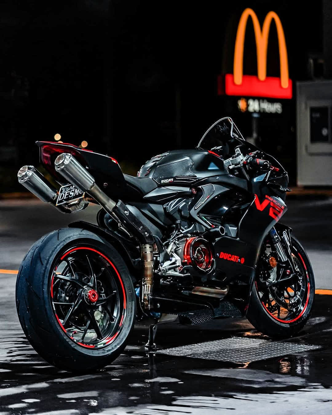 Black Ducati motorcycle with red accents parked on a street at night, McDonald's sign visible in the background.