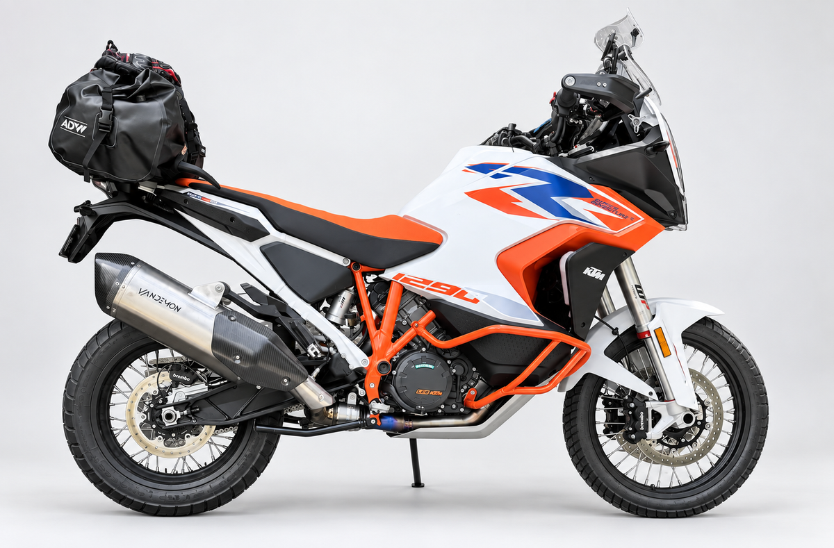 A KTM 400 GS-F dual-sport motorcycle in white, orange, and blue, shown in side profile against a light grey studio background. It is equipped with a black pannier bag on the rear rack and a silver exhaust pipe.
