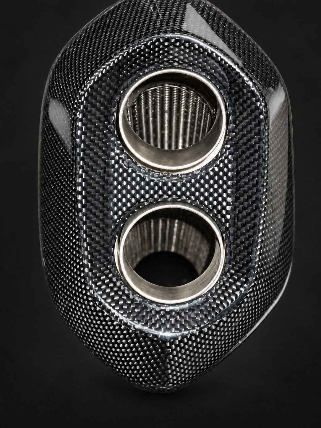 A close-up of a carbon fiber textured automotive part with two circular openings, shown against a dark background.