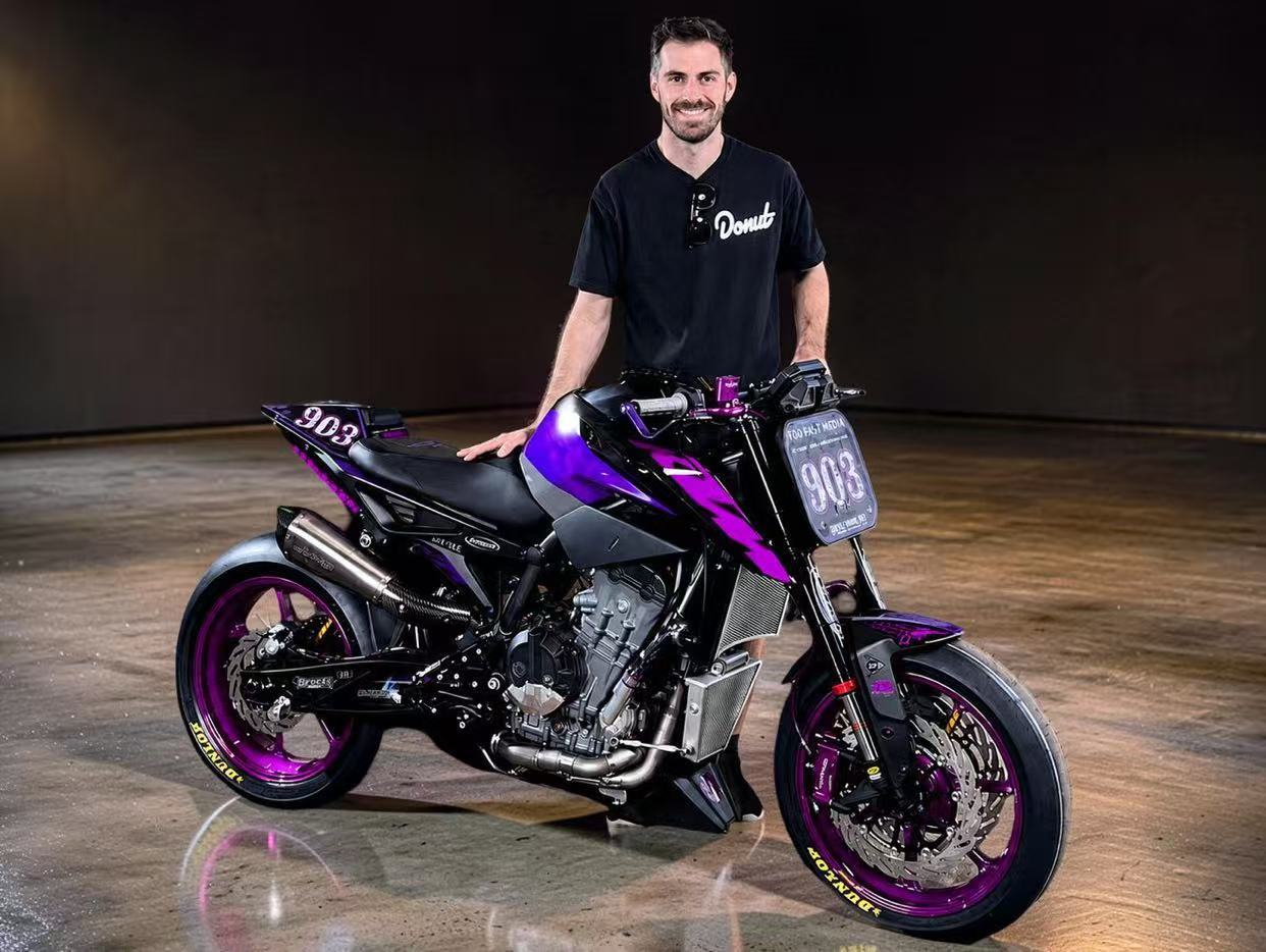 Man standing next to a black and purple motorcycle in a studio setting