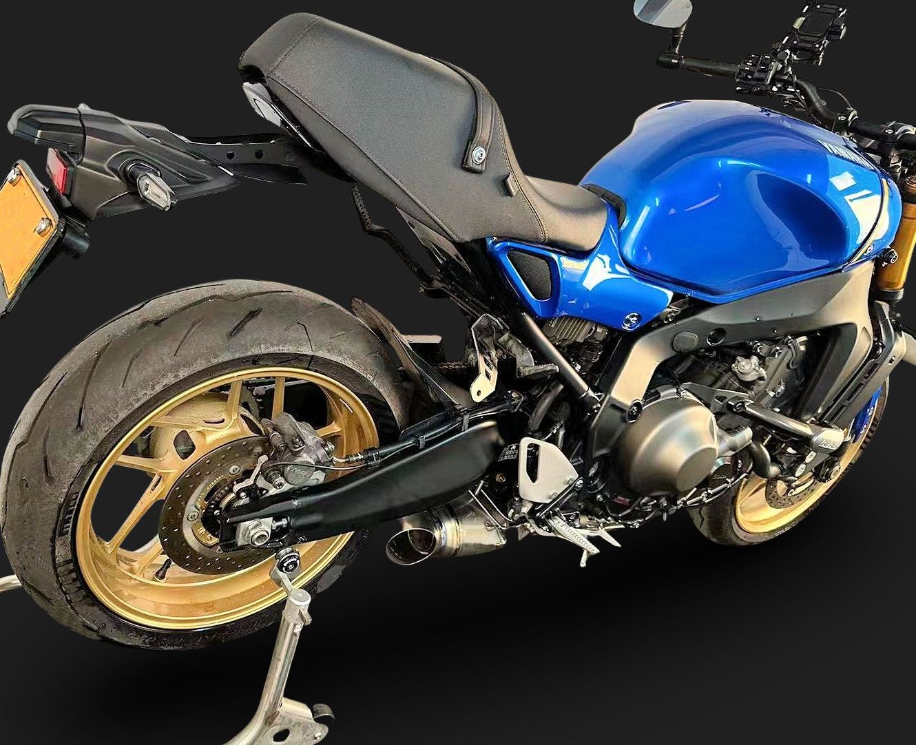 A blue motorcycle with gold rims displayed against a solid black background.
