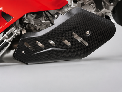 A close-up of a black carbon fiber motorcycle engine guard with cutouts, mounted over a red and silver motorcycle engine.