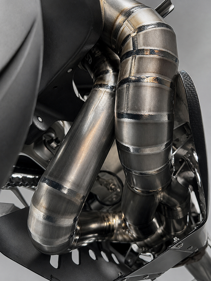 Close-up of a motorcycle exhaust system with polished stainless steel pipes and dark metal components.