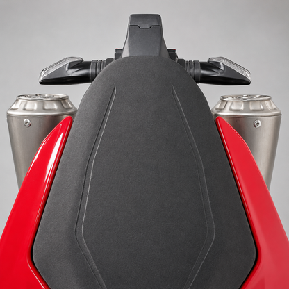 Close-up of a motorcycle's front section showing a black textured seat, silver exhaust pipes, and red body panels against a gray studio background.