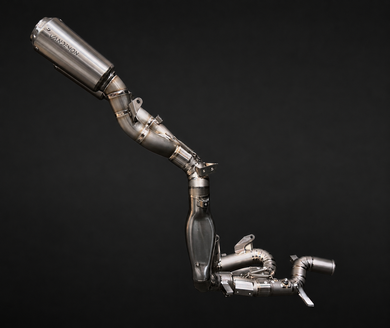A stainless steel automotive exhaust system with a large cylindrical muffler and multiple curved pipes, photographed against a solid black background.