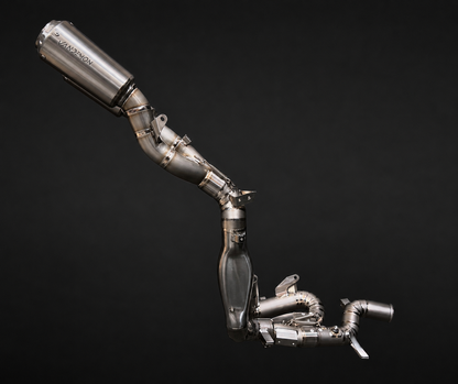 A stainless steel automotive exhaust system with a large cylindrical muffler and multiple curved pipes, photographed against a solid black background.