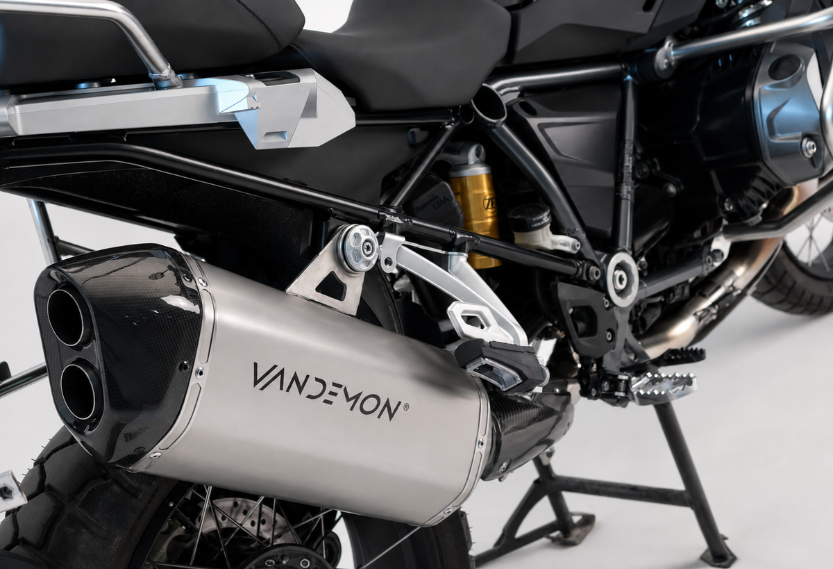 A close-up studio shot of a motorcycle's exhaust system, featuring a prominent silver and black muffler mounted on the side of a black and silver bike.