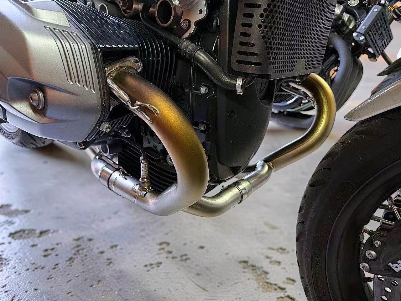 Close-up of a motorcycle engine with gold exhaust pipes on a concrete floor.