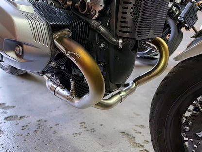 Close-up of a motorcycle engine with gold exhaust pipes on a concrete floor.