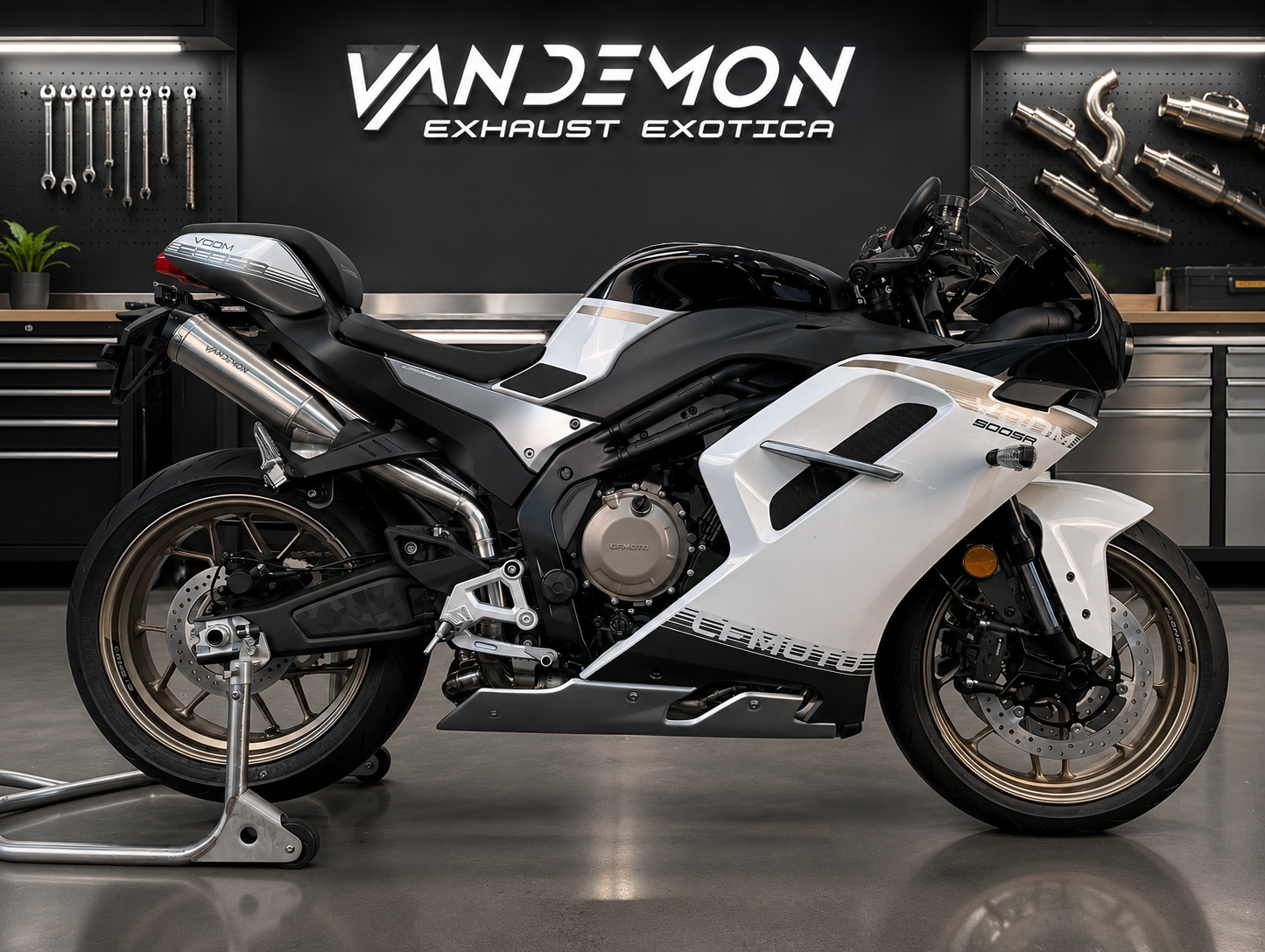 A white and black sport motorcycle with a clear windshield and silver exhaust, displayed on a stand in a workshop setting with the Vandemon Exhaust Exotica branding on the wall.