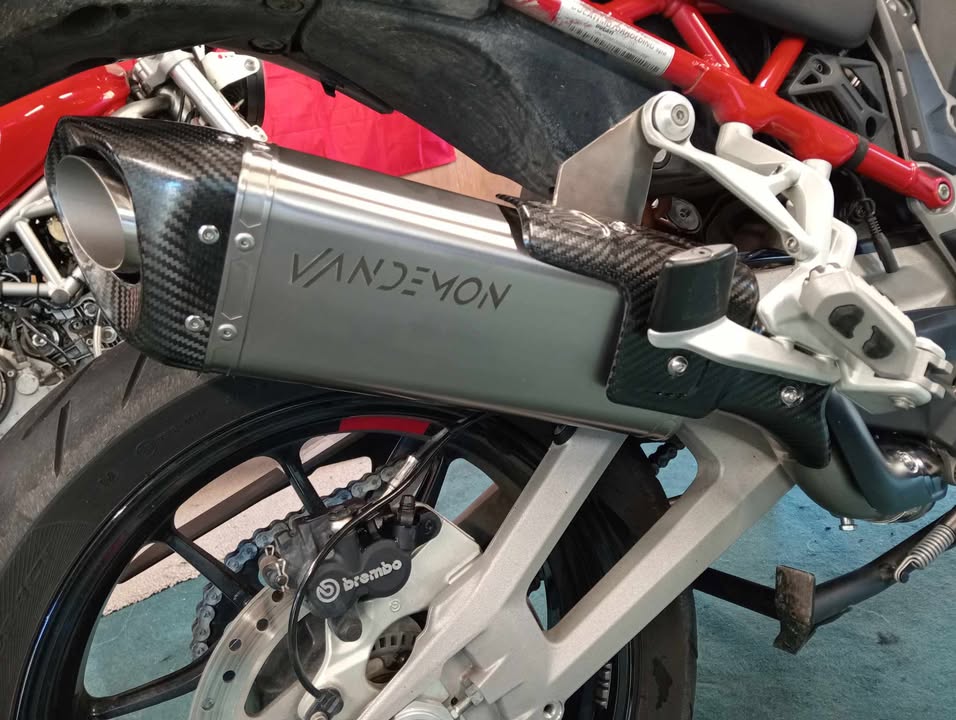 Close-up of a motorcycle exhaust with 'Vandemon' branding on a blurred background