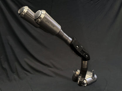 A pair of metallic exhaust pipes with a carbon-fiber joint, positioned vertically against a dark background.