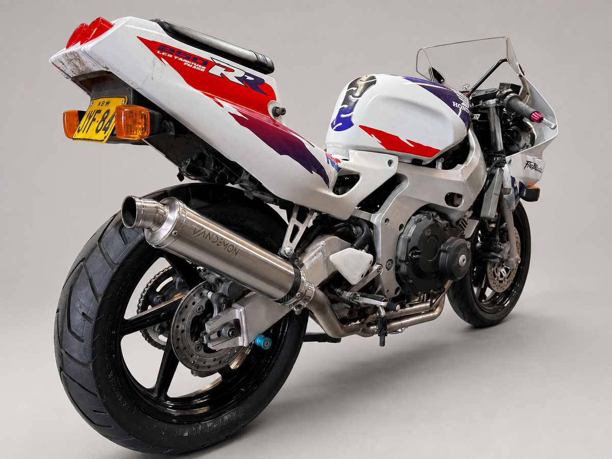 A white Honda CBR sport motorcycle with red and purple graphics, a clear windshield, and a silver exhaust pipe, photographed on a neutral grey studio background.