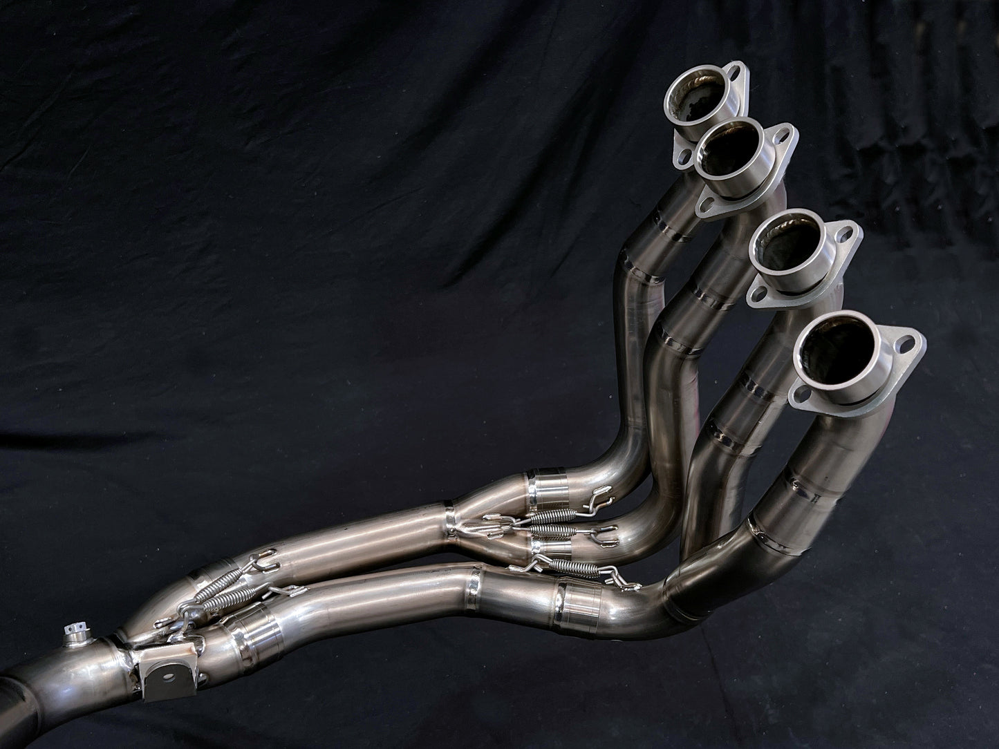 Set of four polished stainless steel exhaust headers with flanged ends and precision bends, converging into a collector.