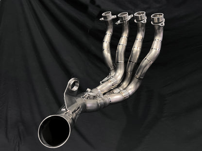 Polished 4-into-1 motorcycle exhaust header with precision welds and flanges, laid out with collector pipe on black backdrop.