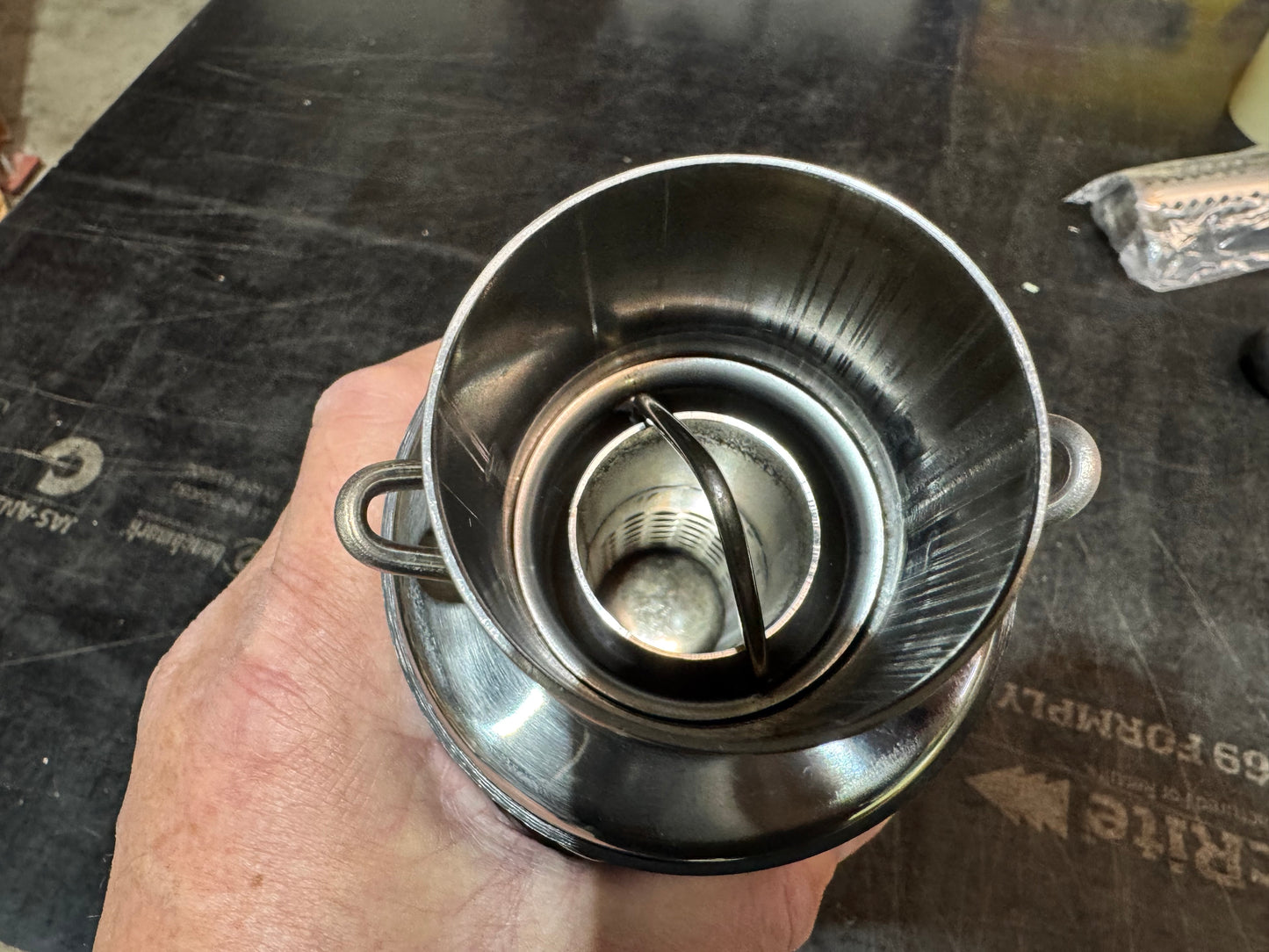 Metal filter held by a hand on a dark surface