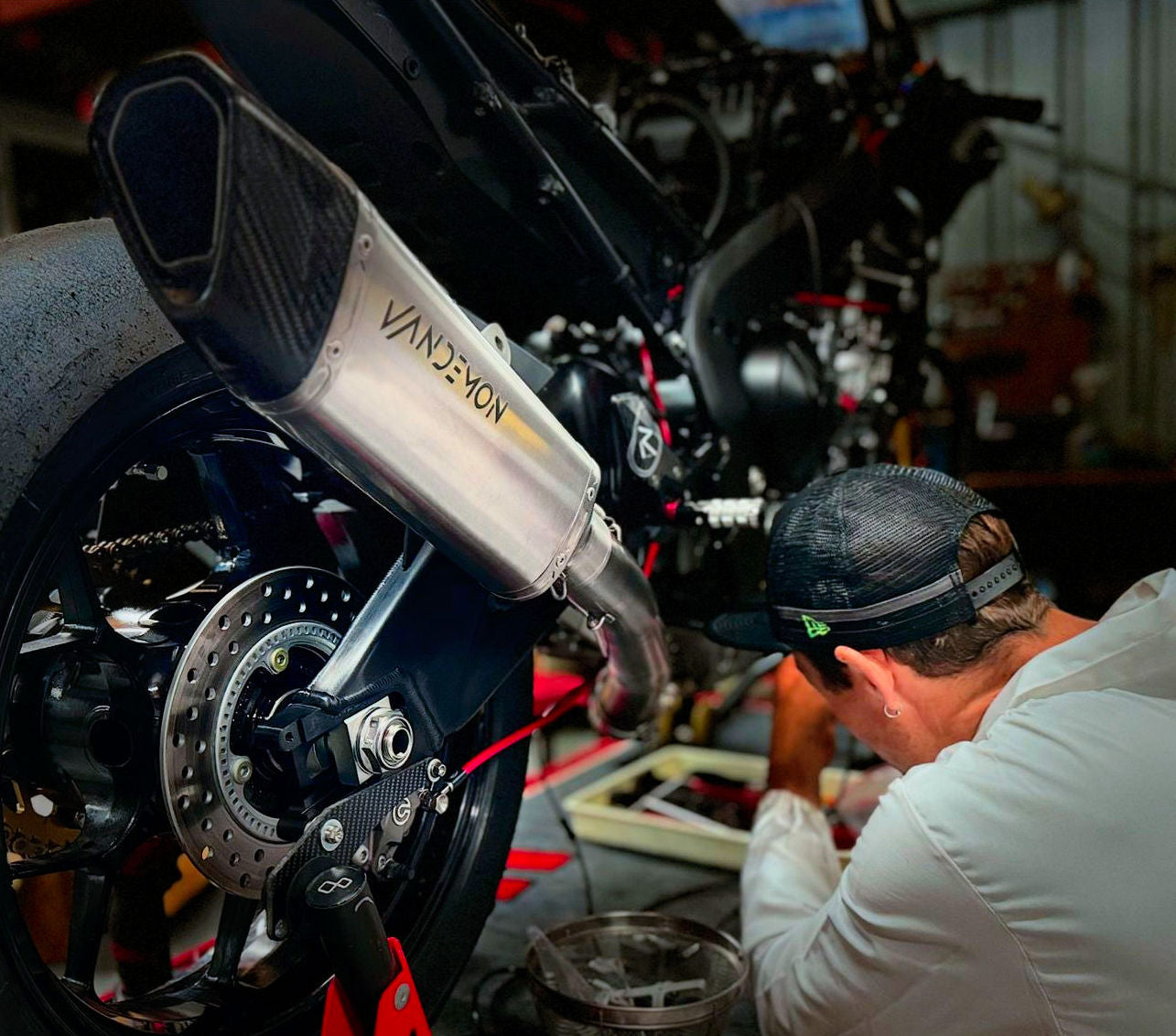 A man is focused on fixing a motorcycle in a garage filled with tools and equipment.