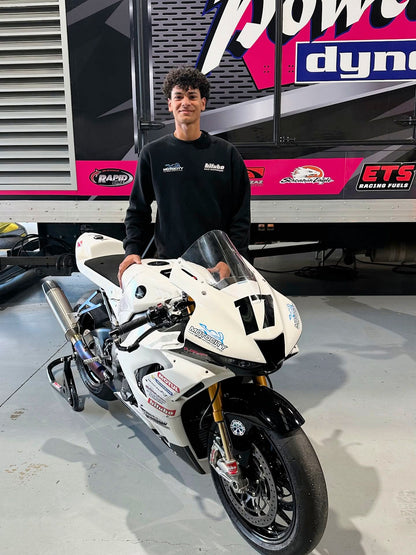 A Man in a black jacket is standing beside a white motorcycle.