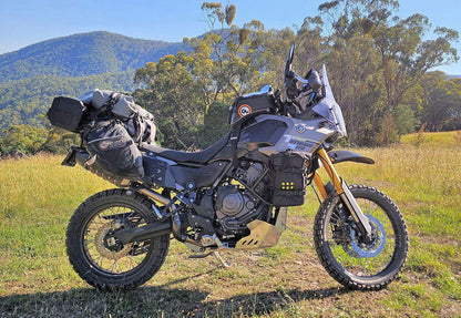 Motorcycle with luggage in a field with mountains and trees in the background